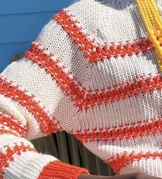 a woman wearing an orange and white sweater holding a yellow beaded necklace in her hand