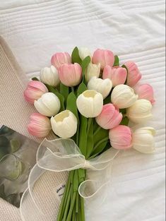 a bouquet of pink and white tulips on a bed with a card next to it