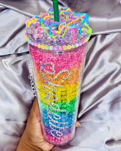 a person holding a colorful cup with a straw in it's mouth and writing on the lid