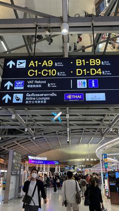 people are walking through an airport terminal with signs on the ceiling and overhead lights above them