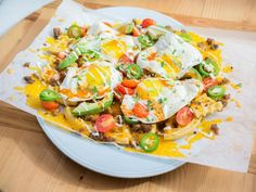 a white plate topped with nachos covered in cheese and toppings on top of a wooden table