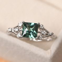 an engagement ring with a green stone surrounded by white diamond accents in a gift box