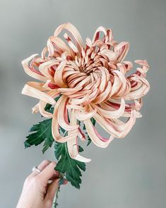 a person is holding a flower made out of strips of ribbon and leaves in their hand