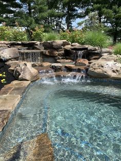 an outdoor swimming pool surrounded by rocks and water features a waterfall that flows into the pond