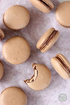 some macaroons are sitting on a white surface and one has a bite taken out of it