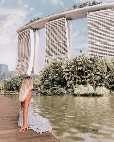 a woman sitting on the edge of a body of water in front of tall buildings