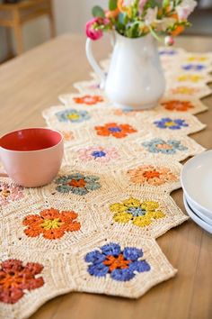 a crocheted table runner on top of a wooden table with plates and cups