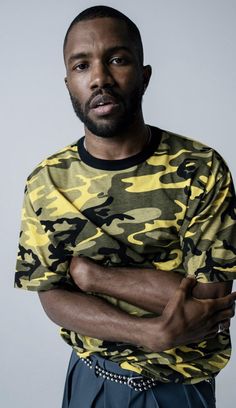 a man with his arms crossed wearing a camouflage t - shirt