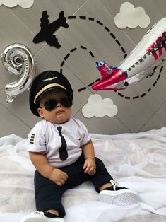 a baby wearing sunglasses and a pilot's hat sitting on top of a bed