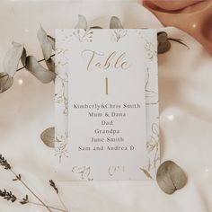 a table number card sitting on top of a white table cloth next to some leaves