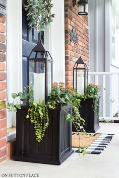 two black lanterns with plants in them on the front porch