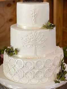 a three tiered white wedding cake with greenery on top