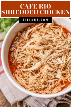 a white bowl filled with shredded chicken on top of a wooden table next to a napkin