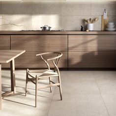 a wooden table and chair in a room with white tile flooring, cabinets and countertops