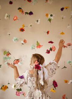 a woman standing in front of a wall covered with paper flowers and holding her hands up to the ceiling