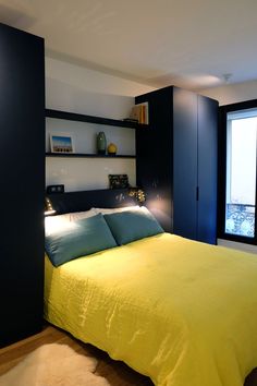 a bed with yellow sheets and blue pillows in a room next to a large window