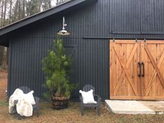 two chairs and a christmas tree in front of a black barn with wooden doors on the side