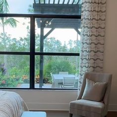 a bedroom with a bed, chair and large window looking out onto the garden outside