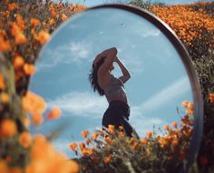 a woman standing in front of a mirror on top of a flower covered field with orange flowers