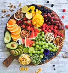 a wooden platter filled with fruits, nuts and fruit salads on top of a white table