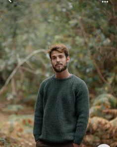 a man standing in the middle of a forest wearing a green sweater and brown pants