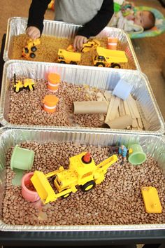 two plastic trays filled with sand and toys on top of a table next to each other