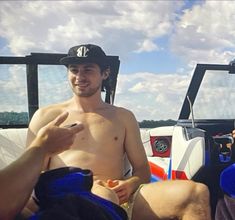 a man with no shirt on sitting in the back of a boat talking to someone