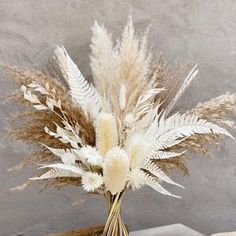 a vase filled with white and brown flowers on top of a wooden table next to a gray wall