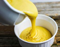 a person pouring yellow sauce into a white bowl