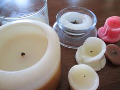 several candles are sitting on a table next to some glass containers and one is empty