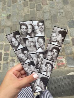 a person holding up several pictures of people in front of a brick wall and sidewalk