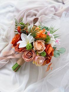 a bridal bouquet with orange, pink and white flowers is laying on a bed