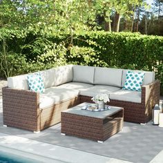 an outdoor furniture set sitting on top of a patio next to a swimming pool with trees in the background