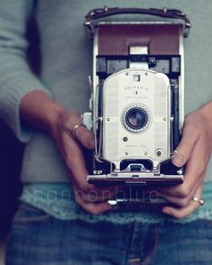 a person holding an old fashioned camera in their hands, taken from the waist up