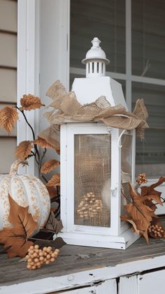 a white lantern sitting on top of a wooden table next to leaves and acorns