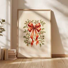 a framed christmas card with a red bow and holly wreath on it next to some books