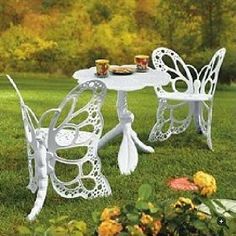 a white table and chairs sitting on top of a grass covered field next to flowers