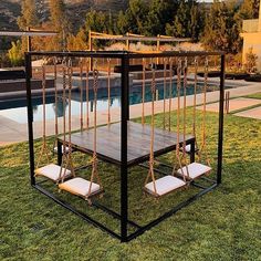 an outdoor swing set in the grass near a swimming pool