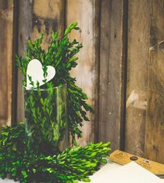 a vase filled with greenery sitting on top of a table next to a piece of paper