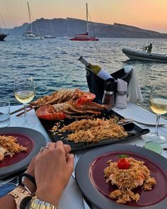 two people are sitting at a table with plates of food and wine glasses on it