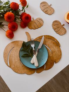 a table set with place settings, flowers and leaves on top of the tablescloth