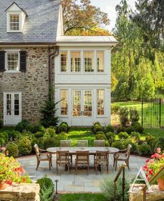 an outdoor dining area in front of a large house with stone walls and white trim