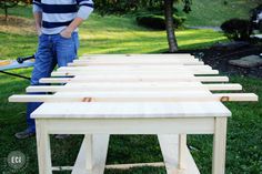 a man standing next to a table made out of wooden planks in the grass