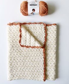 a crocheted blanket with a ball of yarn next to it on a white surface