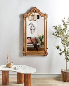 a mirror hanging on the wall next to a table with a vase and potted plant