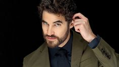 a man with curly hair and beard wearing a green blazer looking at the camera