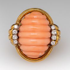 This wonderful cocktail ring is centered with an oval shaped natural coral with a carved fluted design that is set with four-prongs. The coral is bordered to each side with four (4), prong set, round brilliant cut diamonds. The ring measures 28.8mm at the top, rises 18.0mm above the finger, tapering to 2.9mm wide and 1.2mm thick at the base of the shank. It is currently a size 4.75 and is currently unpolished with a rich and lovely patina. Luxury Elegant Coral Rings, Luxury Coral Gemstone Ring, Elegant Oval Coral Rings, Elegant Coral Oval Rings, The Coral, Natural Coral, Pink Coral, Round Brilliant Cut Diamond, Cocktail Ring