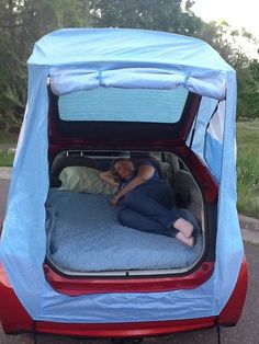 a woman laying on top of a bed in the back of a car with it's door open