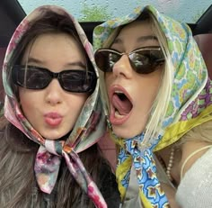 two women in sunglasses and scarfs are sticking their tongue out