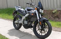 a black motorcycle parked on the side of a road in front of a fence and grass